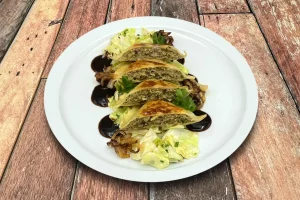 Handgemachte Maultaschen mit geschmortem Spitzkohl und aromatischem Rosmarin-Jus auf einem Teller.